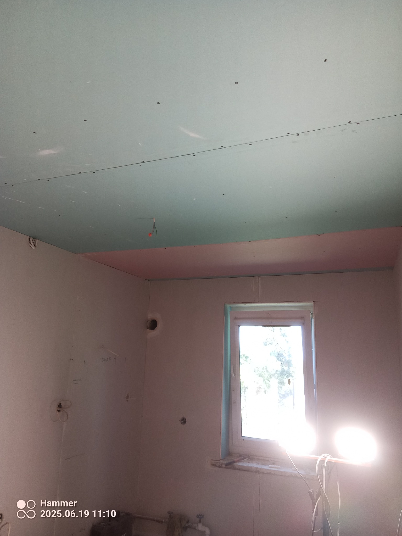 Wnętrze w trakcie prac: sufit z płyt gipsowo-kartonowych, ściany przygotowane do dalszych etapów, okno z widokiem na zewnątrz, oświetlenie robocze.