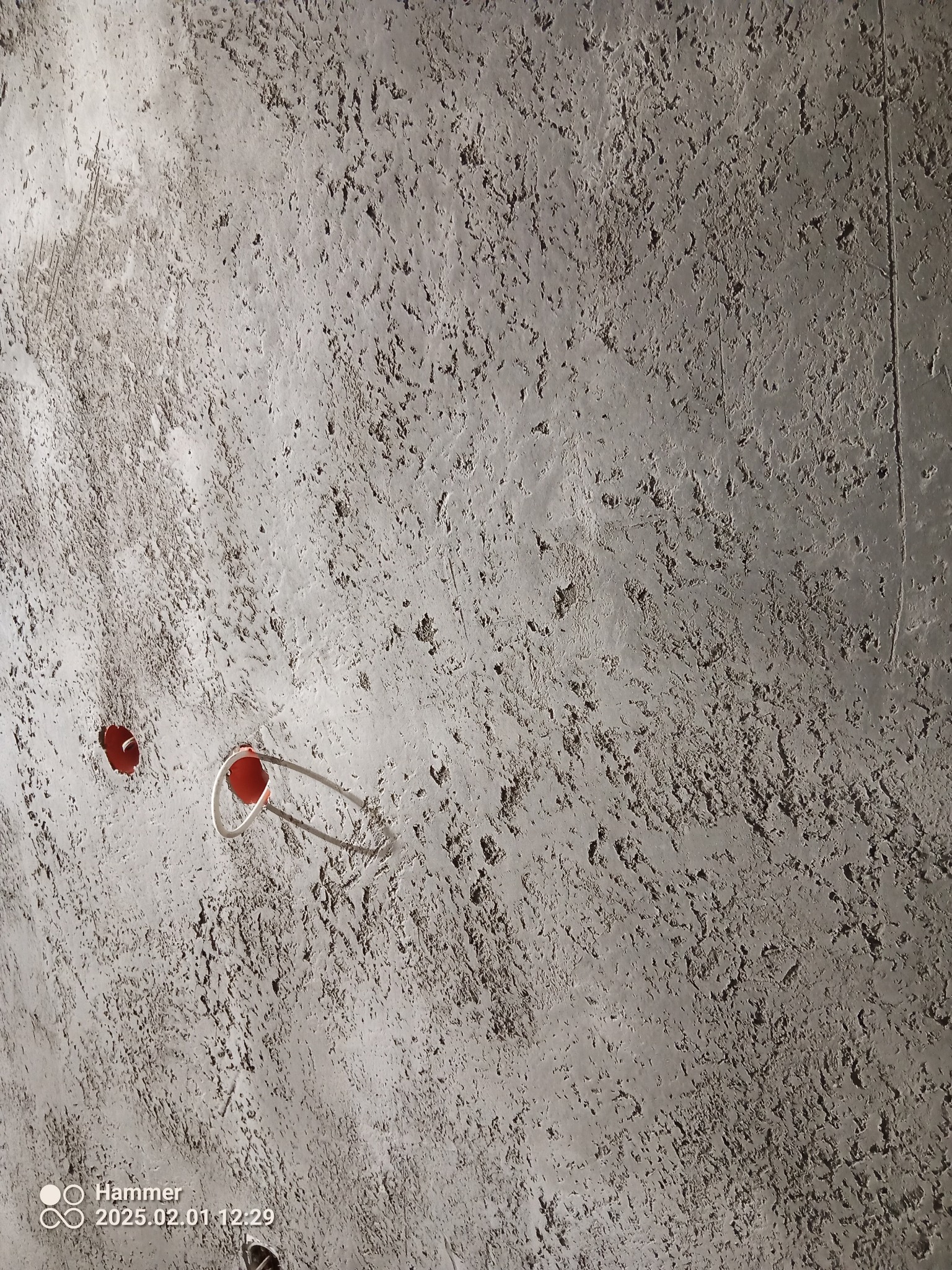 Szara, teksturowana ściana z widocznymi puszkami elektrycznymi. Surowy, minimalistyczny wygląd. Wykończenie z efektem betonu architektonicznego.