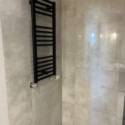 Mariusz Pala - Nowoczesna łazienka z szarymi płytkami i czarnym grzejnikiem drabinkowym. Minimalistyczny design, chromowane zawory.