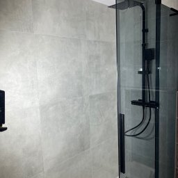 Mariusz Pala - Nowoczesna kabina prysznicowa z czarnymi elementami i szklaną ścianką, wykończona szarymi płytkami w łazience. Minimalistyczny design.