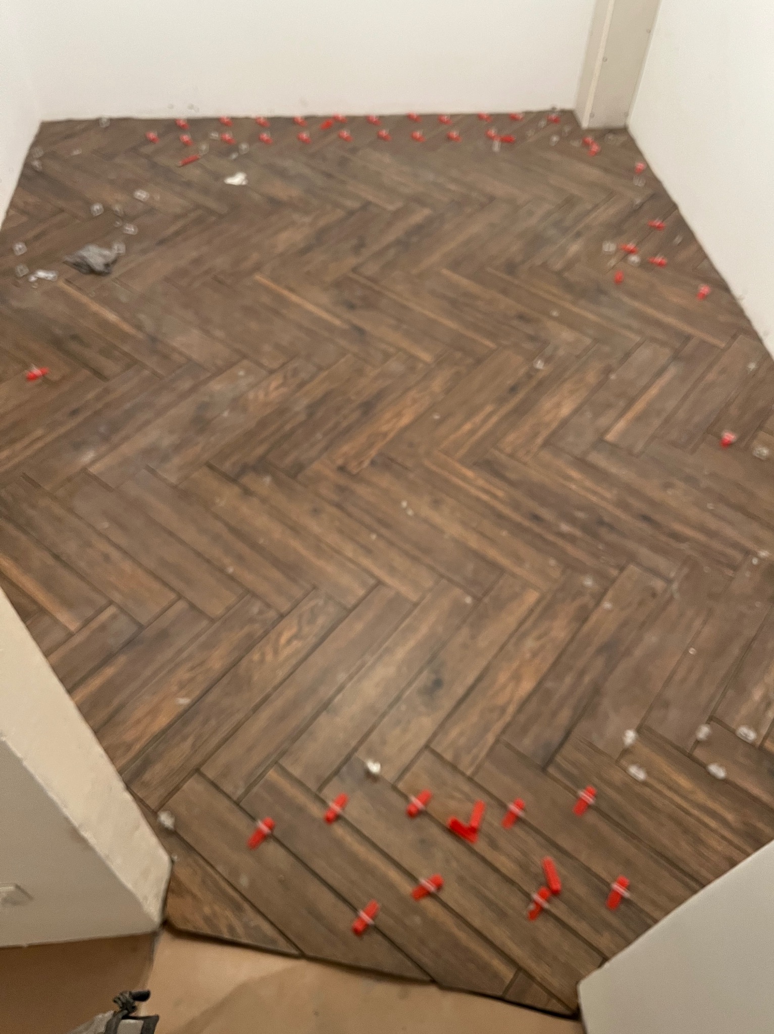 Ukończona podłoga z płytek imitujących drewno, ułożonych w jodełkę, z czerwonymi krzyżykami dystansowymi. Widok z góry, fragment ściany i podłogi w tle.