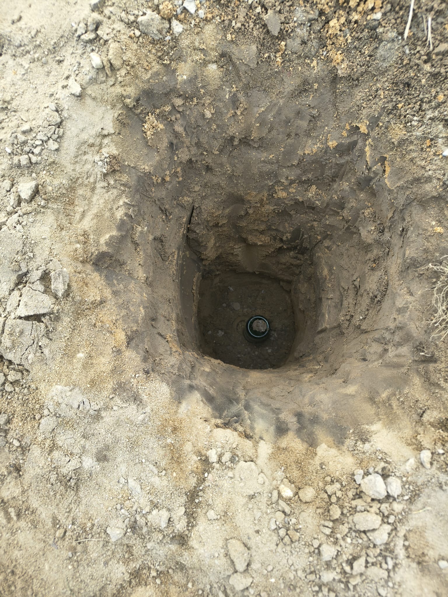 Wykonany odwiert w ziemi z widoczną rurą wewnątrz. Prace ziemne w jasnym oświetleniu, widok z góry na wykopany otwór w gruncie.