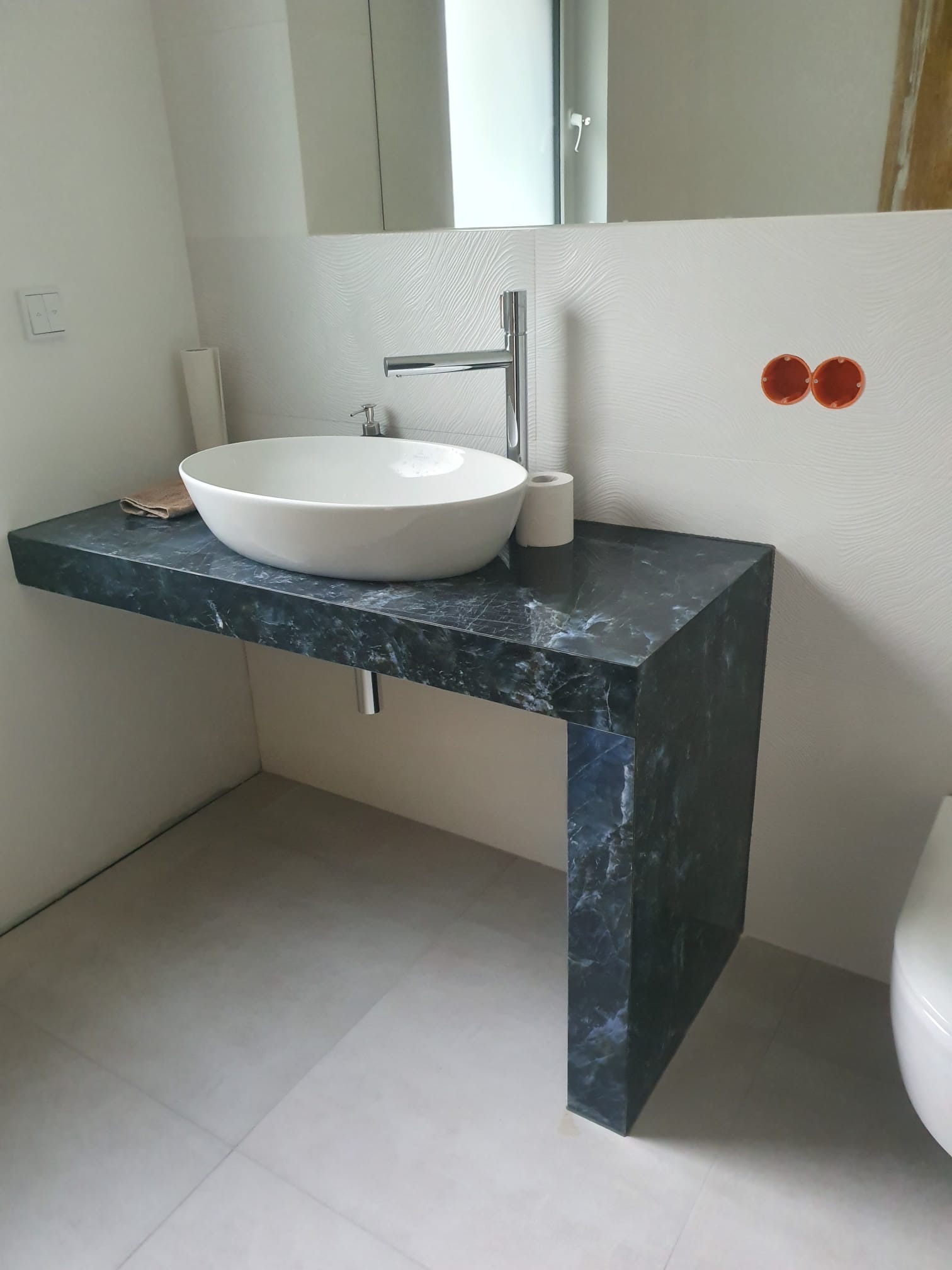 Nowoczesna łazienka z umywalką nablatową na blacie z ciemnego marmuru. Na ścianie dekoracyjna faktura i chromowana bateria.