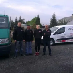 Zespół firmy z dwoma samochodami: zielony z napisem 'Amstutz Gartenbau' i biały z napisem 'Węgiel kamienny, polski i importowany, brykiet rekord'.