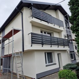 Usługi ogólnobudowlane PROHOUSE - Dwukondygnacyjny dom z balkonami po renowacji elewacji w Brennej. Widoczne rusztowania i drabina, podkreślające etap prac wykończeniowych. Nowoczesne, czarne balustrady.