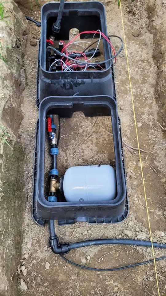 Instalacja systemu nawadniania w ziemi, widoczne elementy w czarnej skrzynce: zbiornik, rury, zawory i przewody elektryczne. Żółta linka wyznacza trasę.