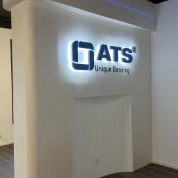 KONOTOP-BUD VIKTOR KONOTOPCHYK - Podświetlane logo 'ATS Unique Banding' na białej ścianie z dekoracyjną wnęką. Nowoczesny design wnętrza biura z elementami wykończeniowymi.