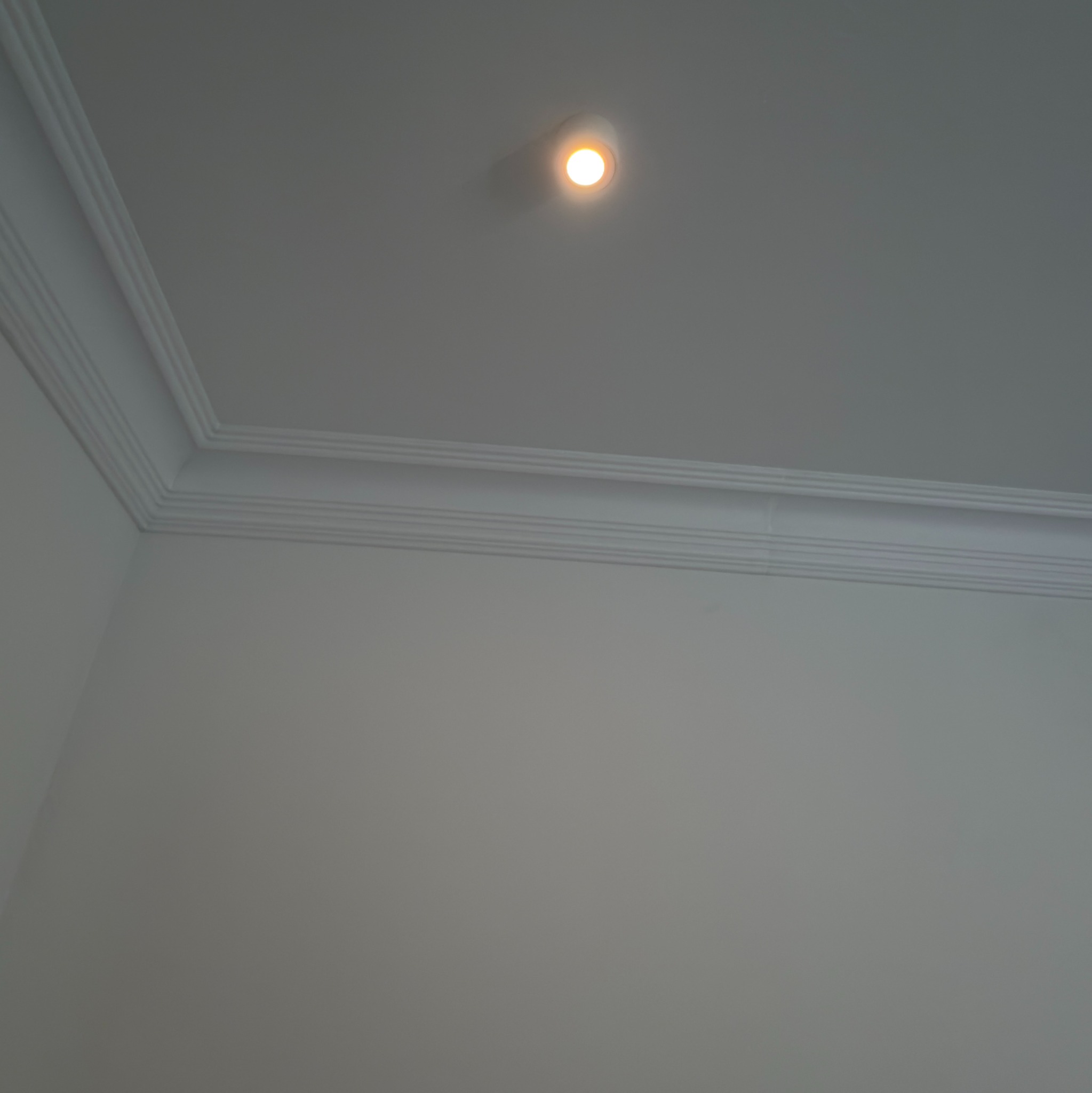 Białe ściany z dekoracyjnym gzymsem sufitowym i punktowym oświetleniem. Minimalistyczne wykończenie wnętrza, widok z dołu.