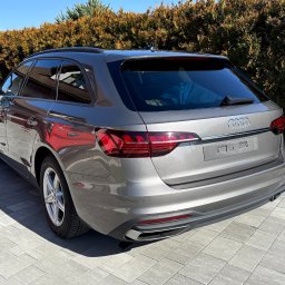 Glossper Auto Detailing - Szary samochód Audi A4 Avant, widok z tyłu na tle żywopłotu. Błyszcząca karoseria po umyciu, czyste felgi i opony. Auto zaparkowane na szarej kostce brukowej.