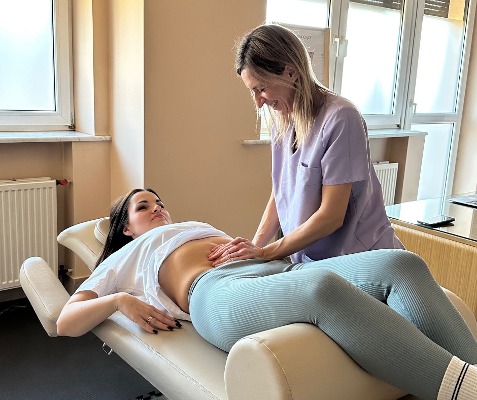 Kobieta w trakcie badania palpacyjnego brzucha przez terapeutkę w gabinecie. Pacjentka leży na specjalistycznym łóżku, terapeutka w uniformie pochyla się nad nią.