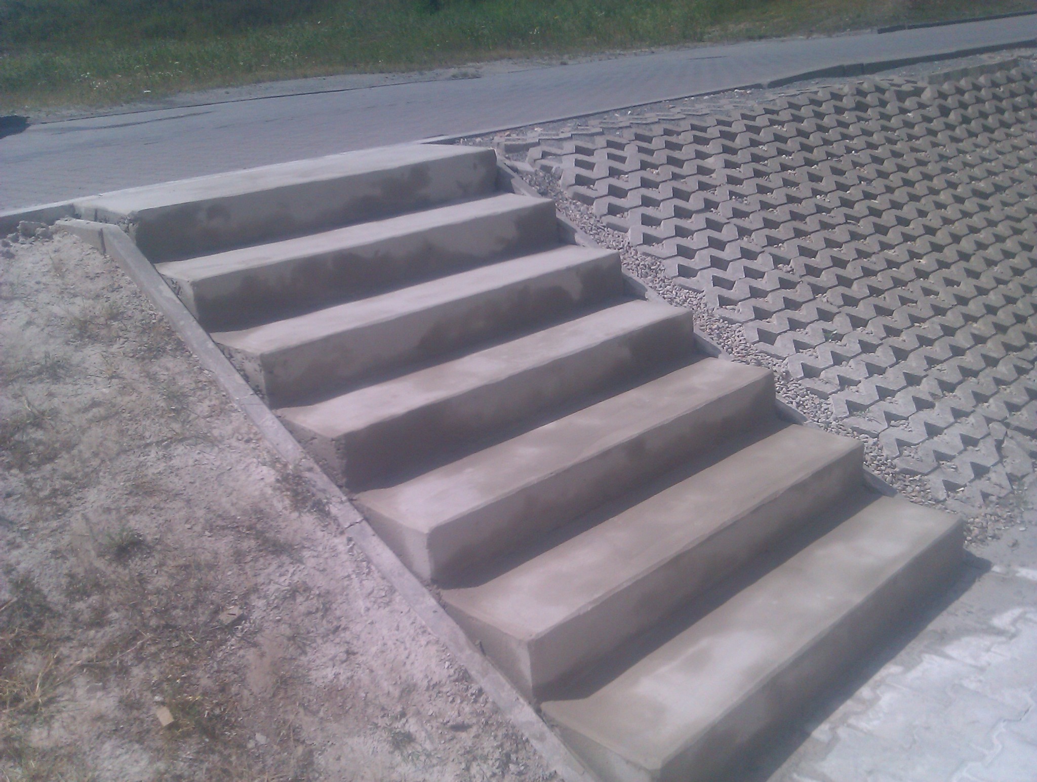 Betonowe schody zewnętrzne z kostką ażurową w tle, widok z boku. Nowoczesne rozwiązanie architektoniczne, solidne wykonanie.