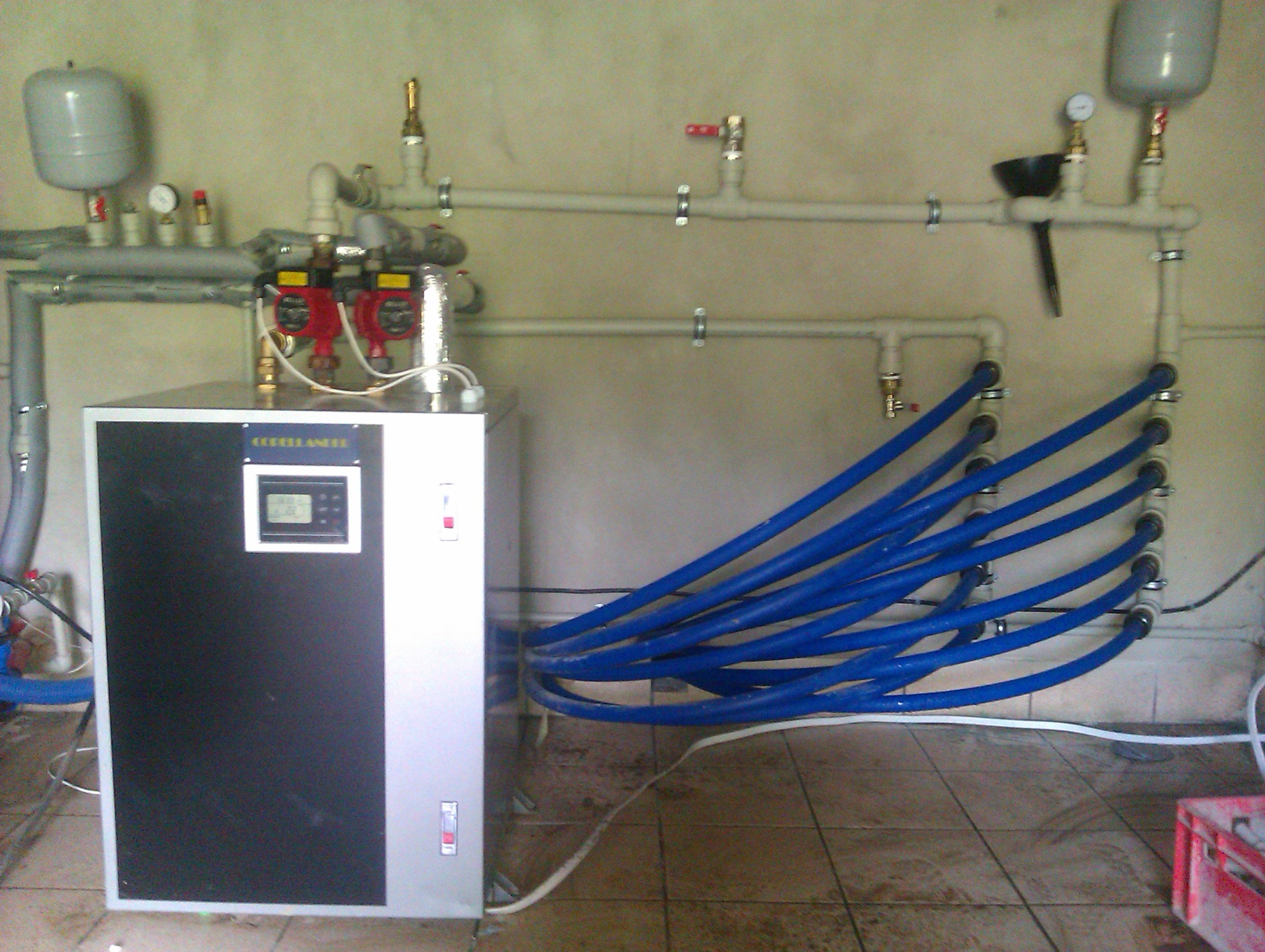 Kompaktowa centrala rekuperacyjna z podłączonymi niebieskimi rurami wentylacyjnymi i instalacją. Widoczne pompy obiegowe i manometry.