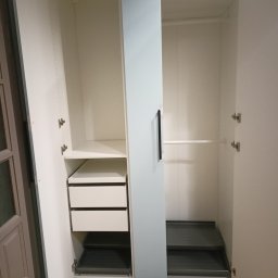 Montaż mebli paczkowanych Usługi transportowe - Wnętrze szafy wnękowej z szufladami i półkami, widok z otwartymi drzwiami. Białe wykończenie, minimalistyczny design, metalowe okucia.