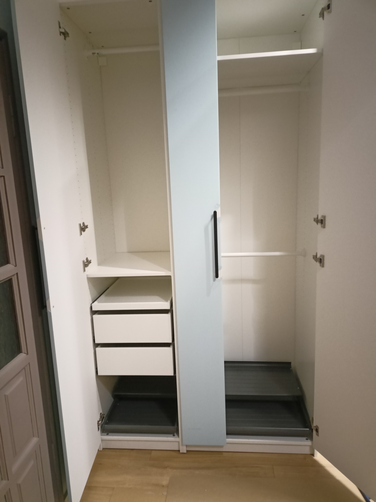 Wnętrze szafy wnękowej z szufladami i półkami, widok z otwartymi drzwiami. Białe wykończenie, minimalistyczny design, metalowe okucia.