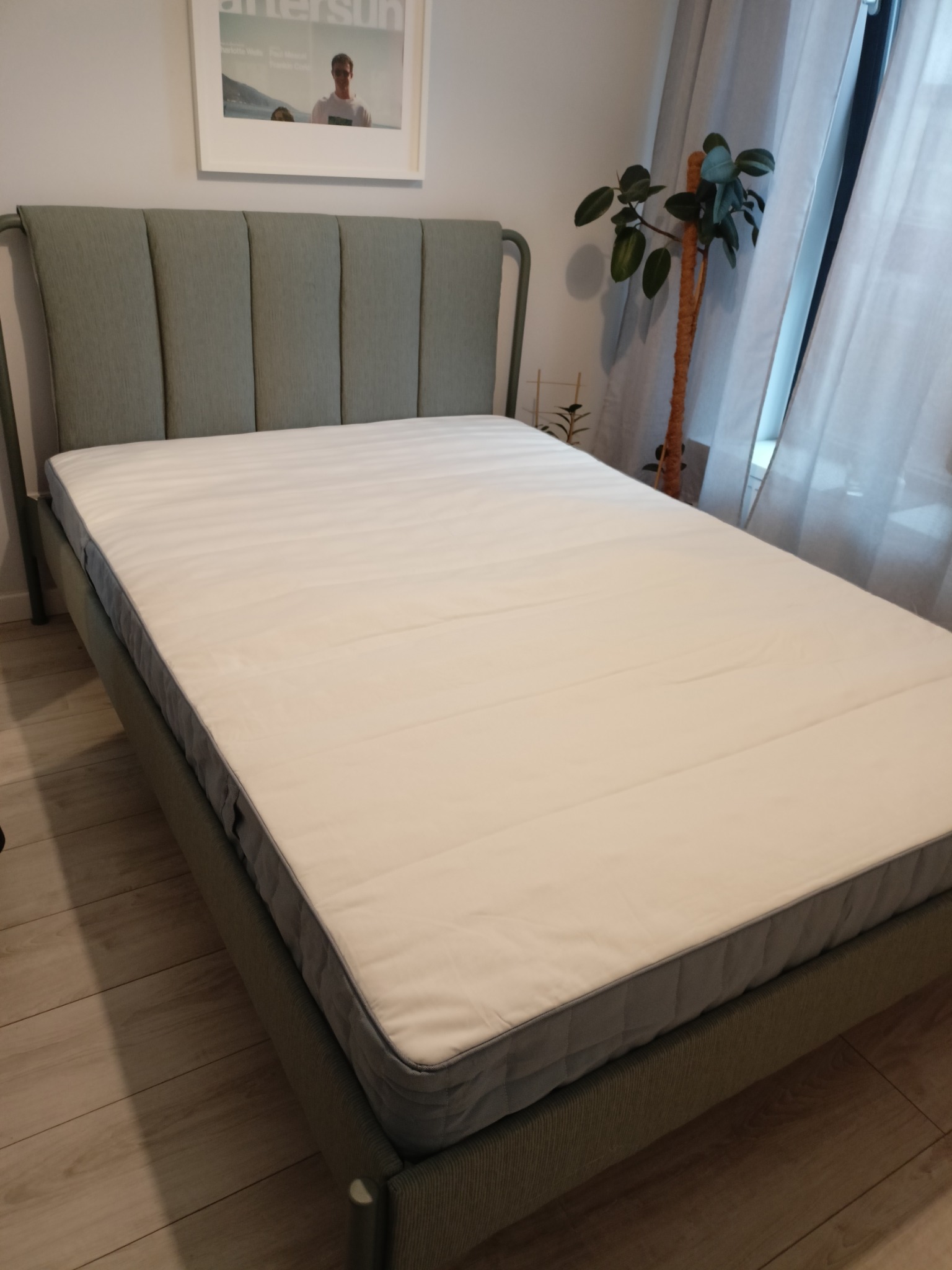 Nowoczesne łóżko z zagłówkiem w odcieniach szarości, ustawione w sypialni w Grodzisku Mazowieckim. Minimalistyczny design, roślina doniczkowa w tle.