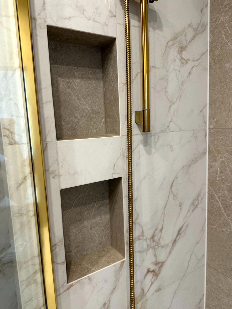 Wykończona wnęka prysznicowa z marmurowymi płytkami i złotym wykończeniem, prezentująca estetyczne i funkcjonalne rozwiązanie do przechowywania w łazience.