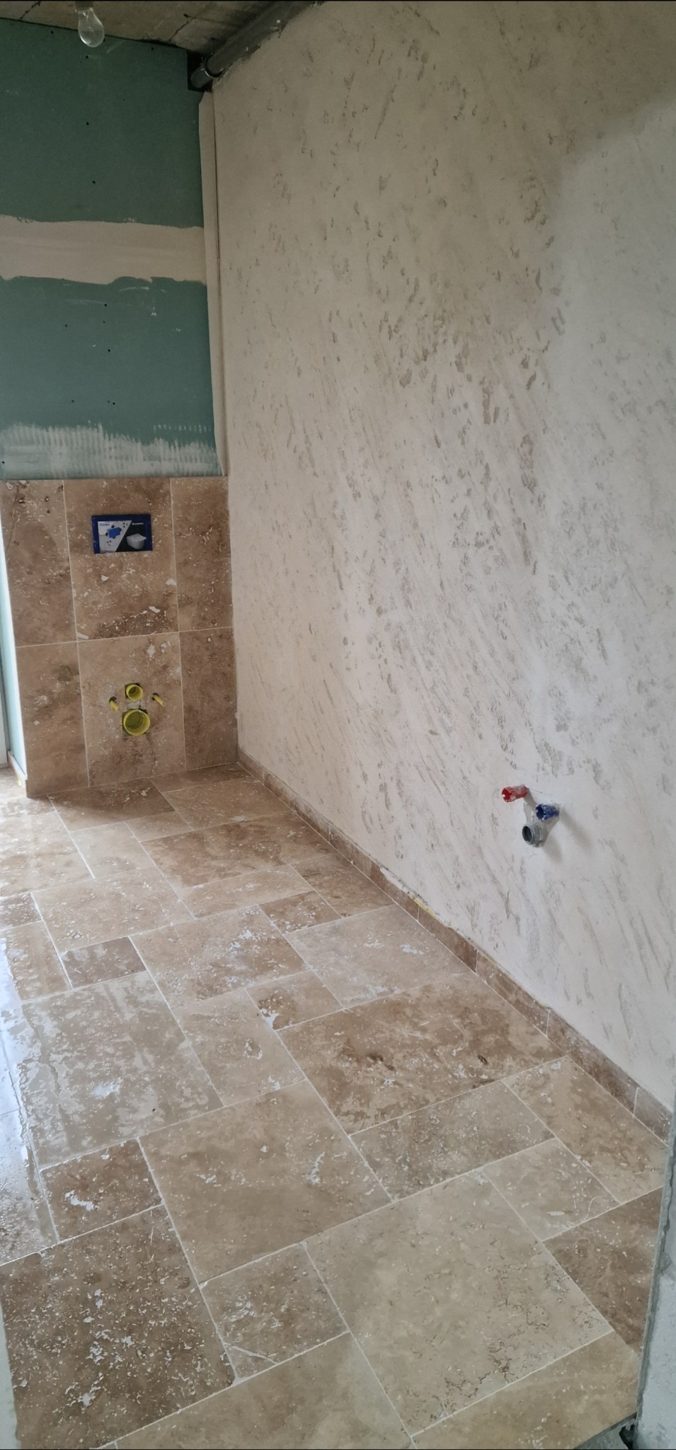 Wykończona łazienka w Gryfowie Śląskim z beżowymi płytkami na podłodze i ścianach. Widoczne przyłącza wodne i fragment ściany z płytą karton-gips.