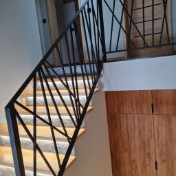 METAL PROCESSING KATARZYNA PROKOP-DZIEDZIC - Nowoczesne schody z podświetleniem LED i czarną, geometryczną balustradą. Widoczne drewniane stopnie i drzwi z motywem kratki w tle. Minimalistyczny design.