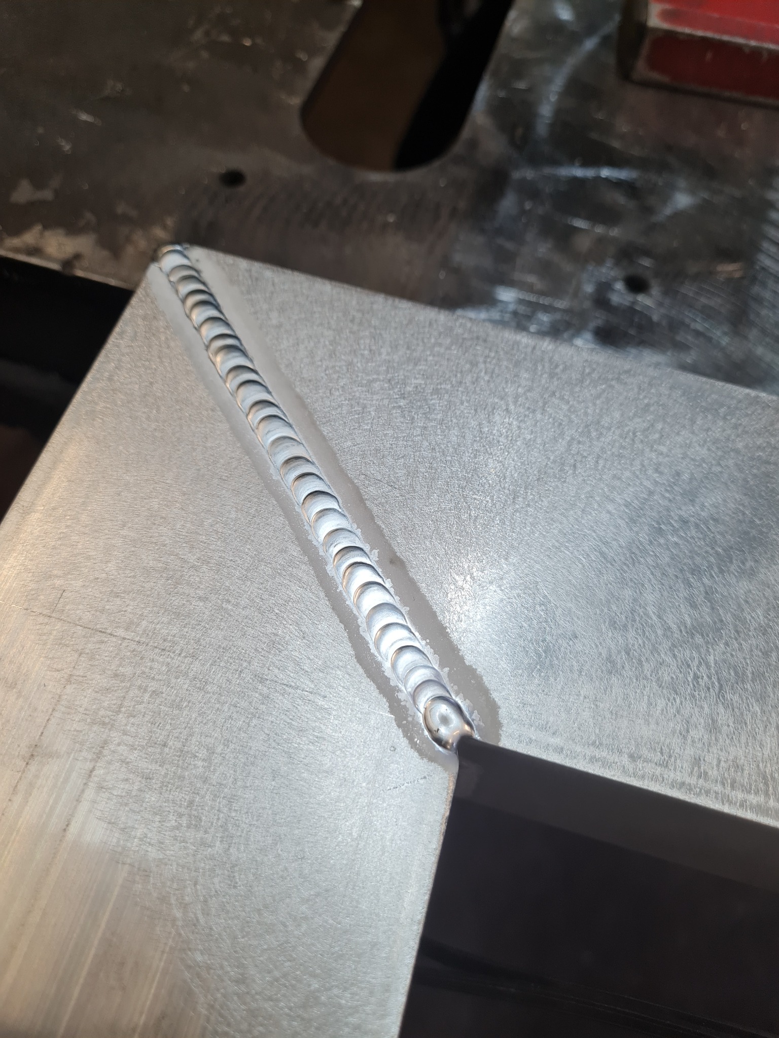 Precyzyjny spaw na metalowej płycie, widoczny z bliska. Regularne, srebrzyste spoiwo tworzy estetyczną linię na szlifowanej powierzchni. Detal spawalniczy.