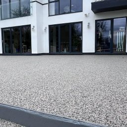 Zywice.pro - Nowoczesny taras z żywicy epoksydowej w odcieniach szarości, przylegający do białego budynku z dużymi, przeszklonymi drzwiami. Minimalistyczny design.