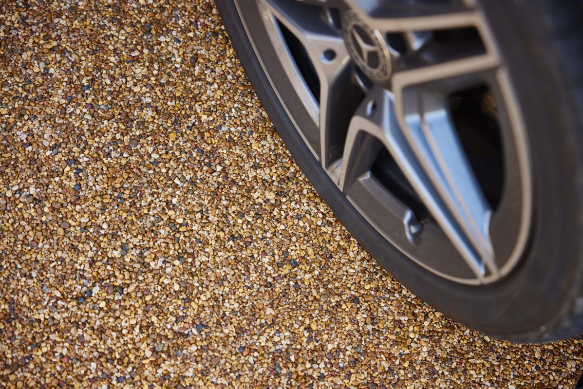 Żwirowa nawierzchnia tarasu z fragmentem koła samochodu, ukazująca detale i teksturę kamiennego dywanu w bliskim ujęciu. Widoczny wzór i kolorystyka drobnych kamyczków.