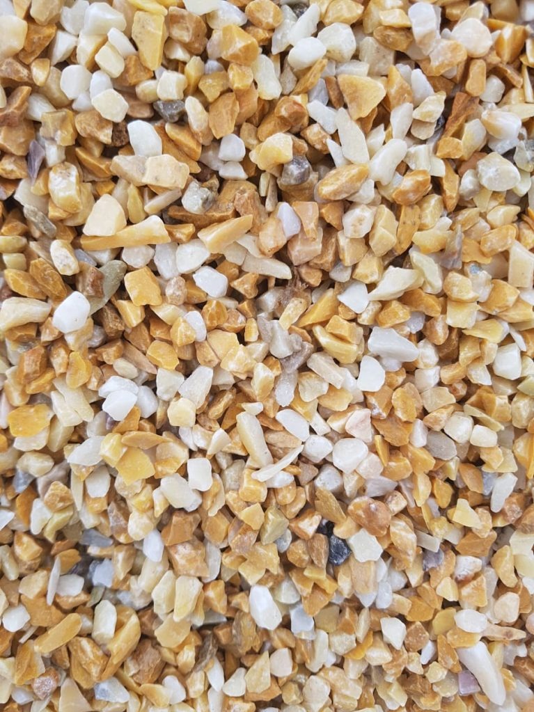 Drobne, nieregularne kamyczki w odcieniach bieli i złota, tworzące teksturę. Idealne do dekoracji tarasu lub ogrodu, z bliska ukazujące naturalne piękno.