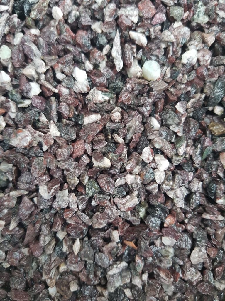 Ciemne, drobne kamienie o nieregularnych kształtach, z przewagą odcieni czerwieni, brązu i szarości. Widoczne pojedyncze białe kamyczki. Bliski kadr.