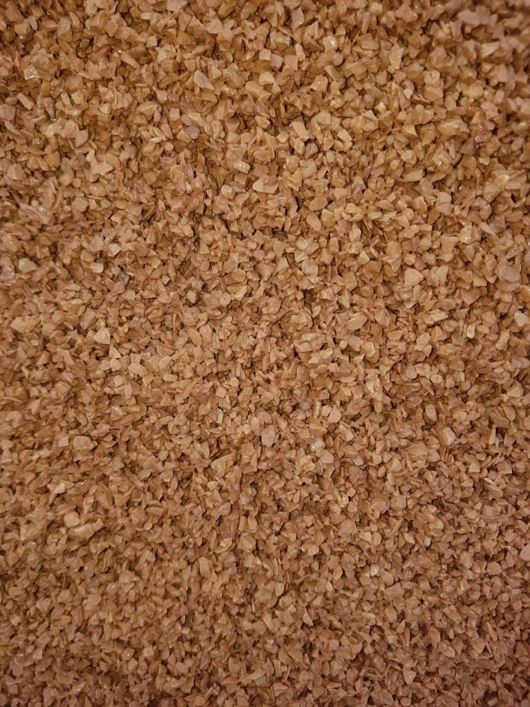 Detale brązowego kruszywa kamiennego o nieregularnych kształtach, wypełniającego kadr. Widoczne drobne nierówności i załamania światła na powierzchni kamieni.