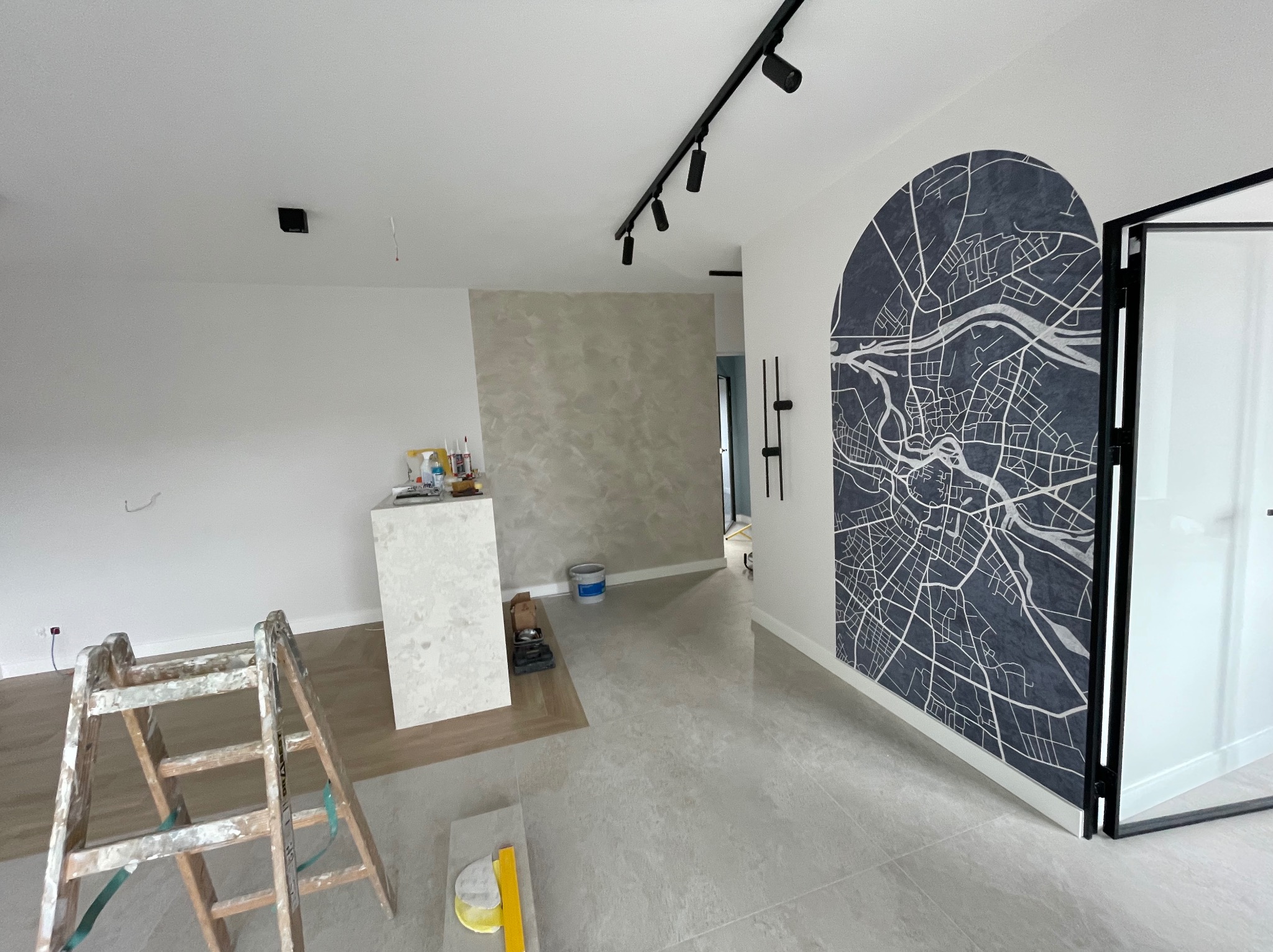 Wykończone wnętrze biurowe z mapą miasta na ścianie, widoczne płytki podłogowe, drabina malarska i oświetlenie sufitowe. Adaptacja pomieszczeń biurowych w Gdyni.