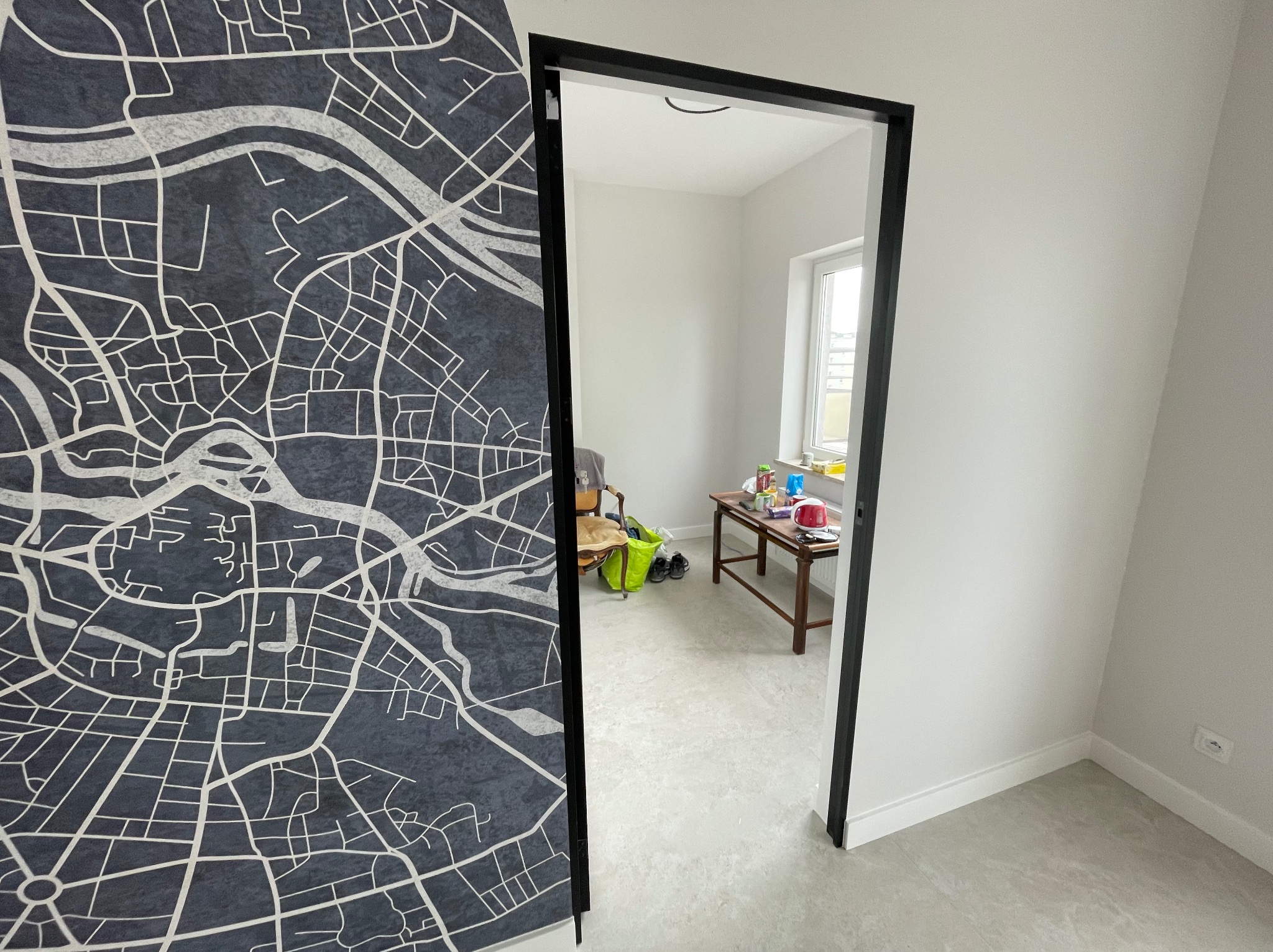 Nowoczesne drzwi przesuwne z mapą w biurze, widok na jasne wnętrze z oknem. Minimalistyczny design, szara podłoga, białe ściany. Adaptacja pomieszczeń biurowych.