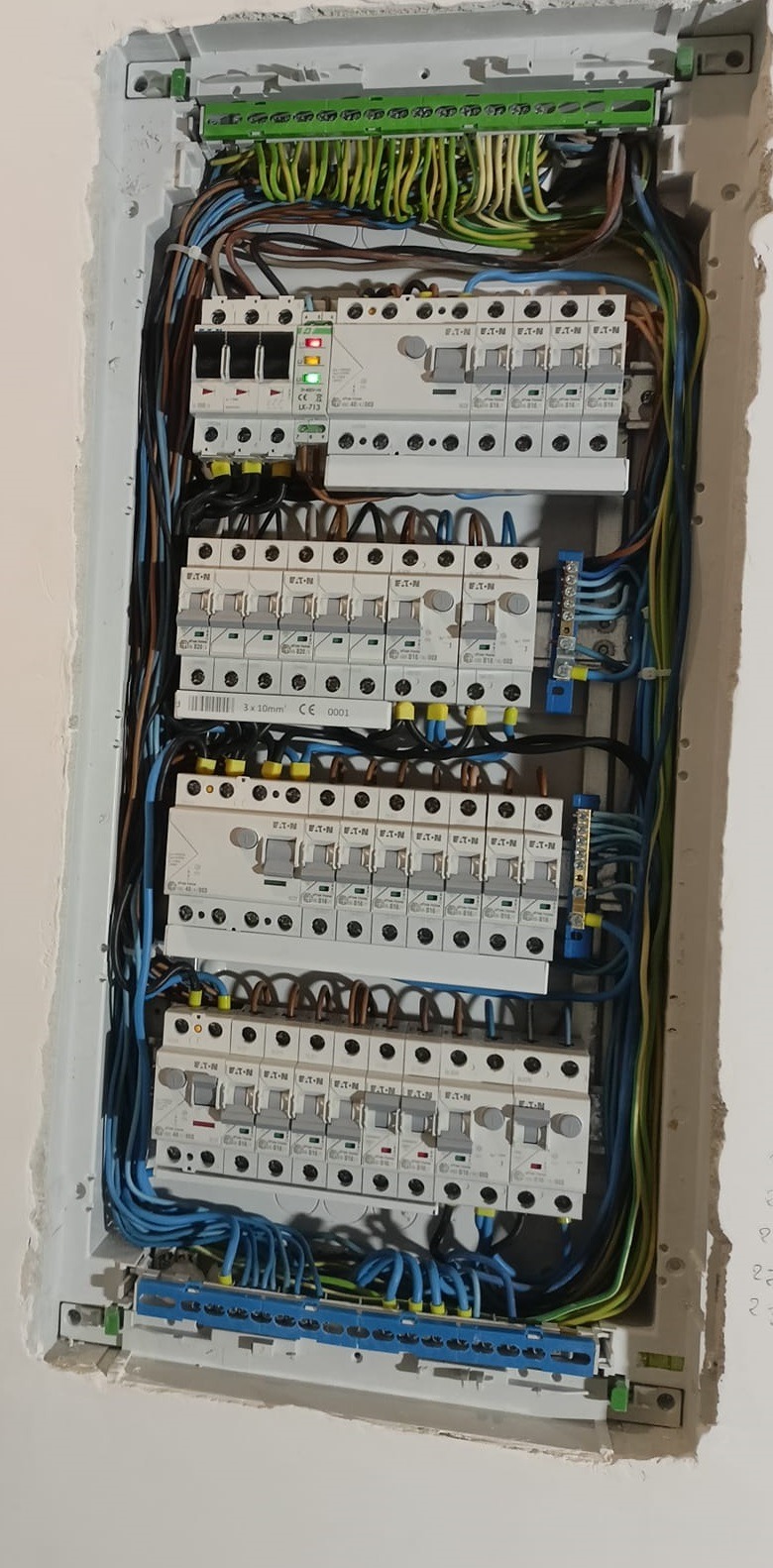 Rozdzielnica elektryczna z bezpiecznikami i przewodami wewnątrz obudowy, widok z bliska na instalację w trakcie prac. Elementy marki Eaton.