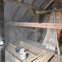 Sebastian Jan - Stare poddasze z drewnianą konstrukcją, widoczne narzędzia i materiały budowlane. Fragment okna z logo Drutex po lewej. Przygotowania do remontu.