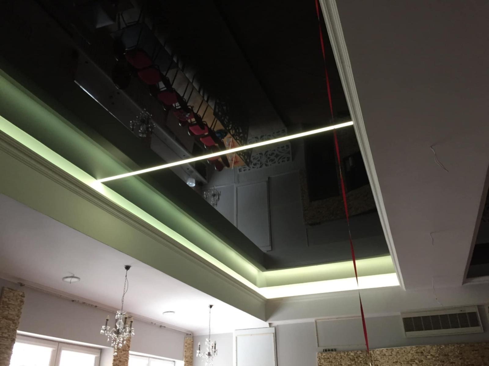 Błyszczący, czarny sufit napinany z oświetleniem LED, odbijający wnętrze pomieszczenia. Widoczne żyrandole i dekoracyjne kolumny.