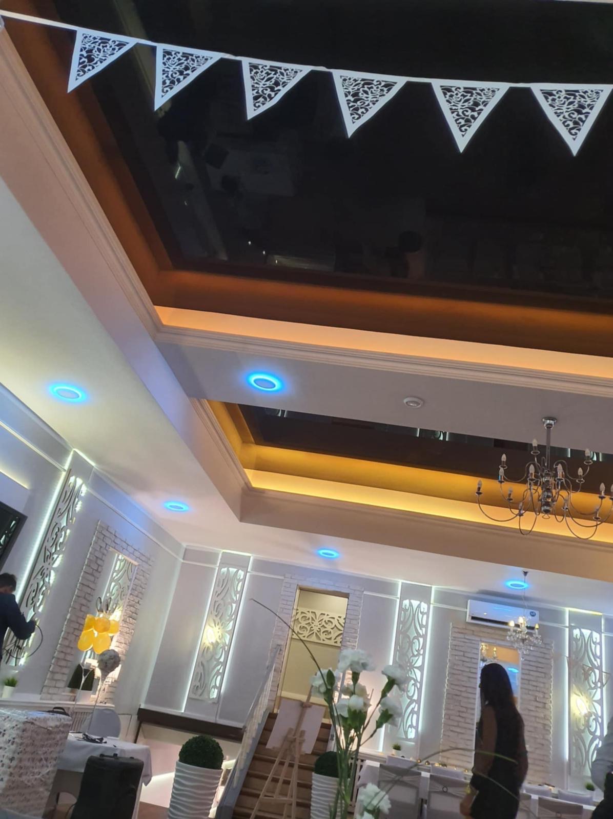 Eleganckie wnętrze sali bankietowej z dekoracyjnymi panelami ściennymi, oświetleniem LED i ozdobnym sufitem podwieszanym. Widoczne detale wykończenia i dekoracje.