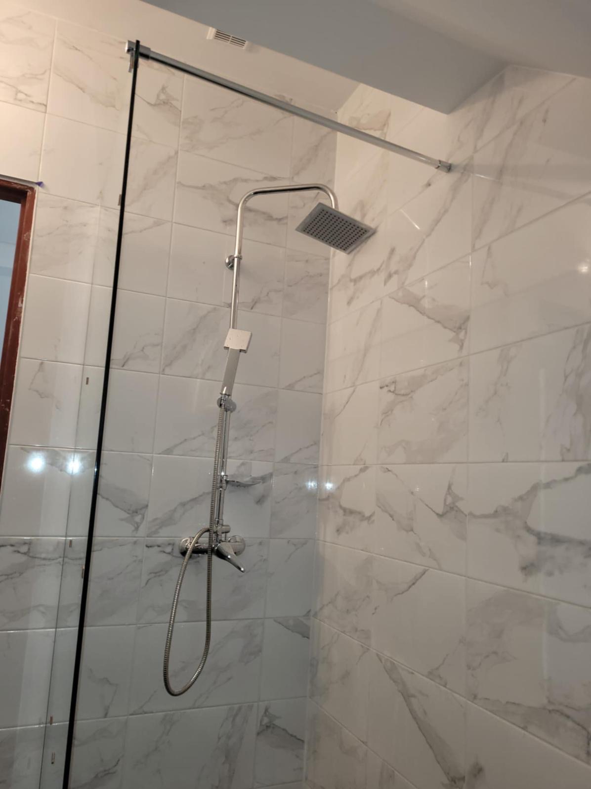 Wykończona kabina prysznicowa z deszczownicą i szklanym panelem, białe płytki imitujące marmur w Margonin. Nowoczesny design łazienki po remoncie.