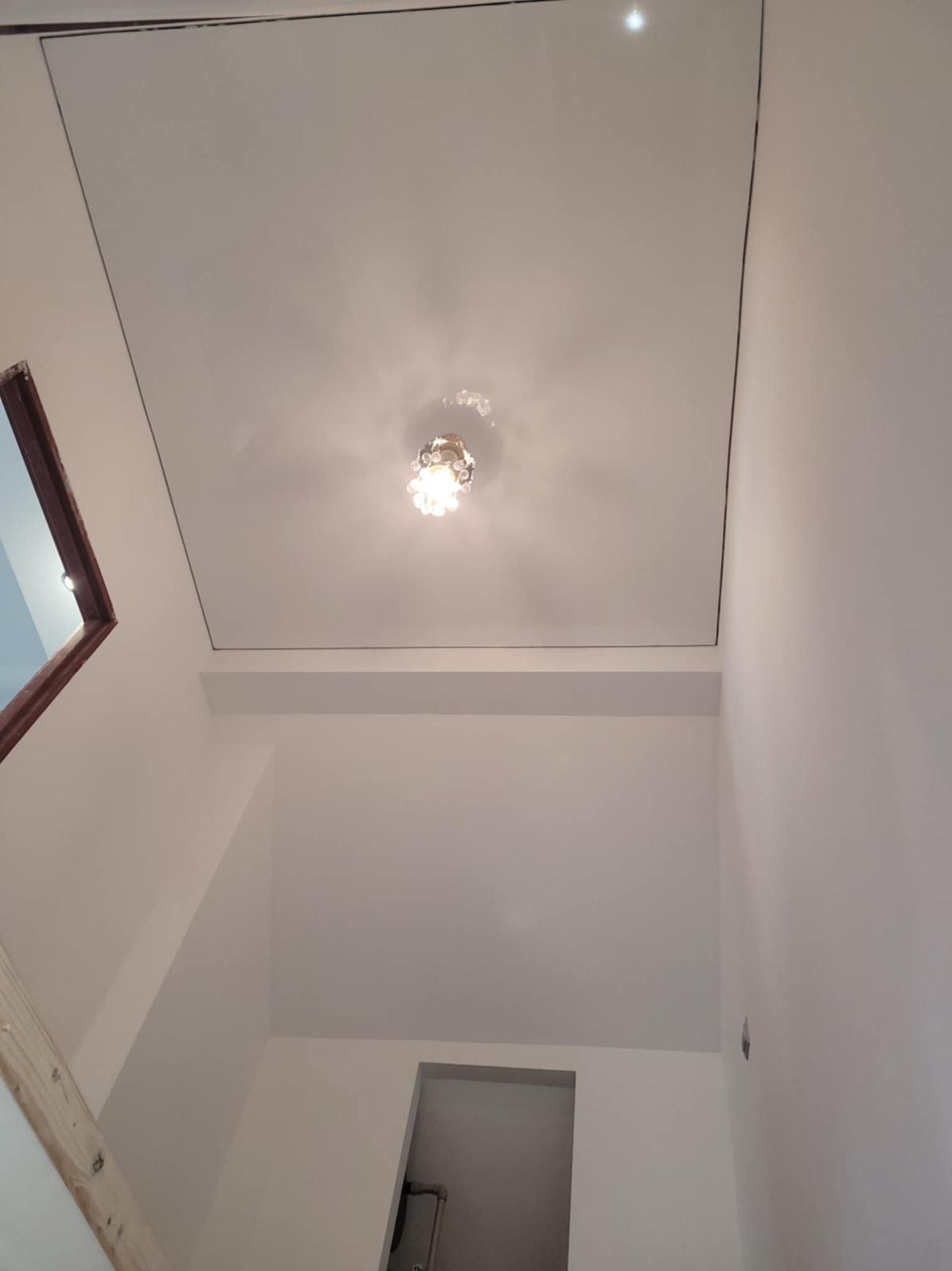 Białe wnętrze po remoncie: gładki sufit z lampą, świeżo pomalowane ściany, widok z dołu. Minimalistyczny design, jasne oświetlenie, czyste linie.