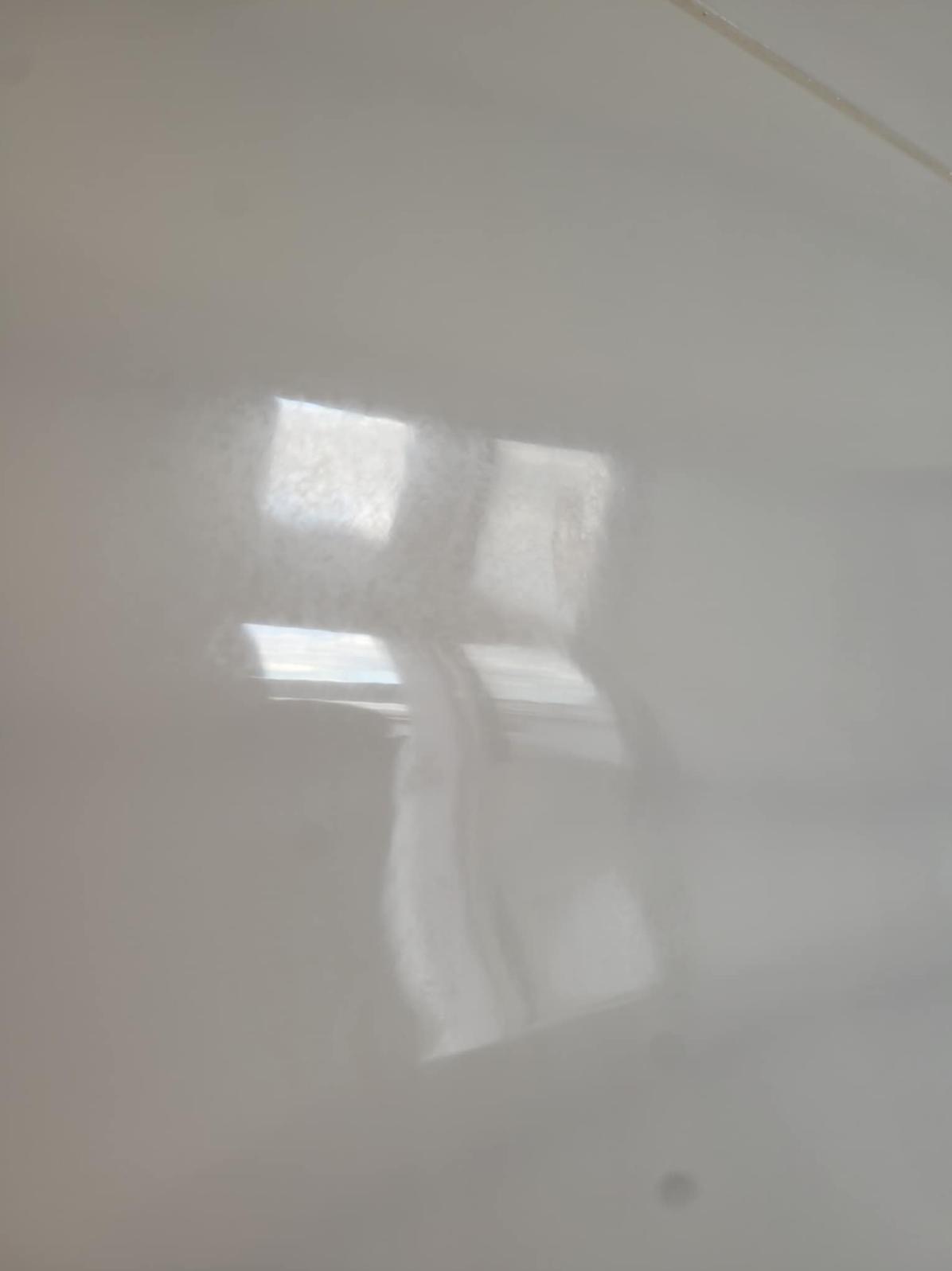 Błyszcząca, jasnoszara powierzchnia z refleksami okien. Widoczne delikatne smugi i niedoskonałości, sugerujące świeżo pomalowaną ścianę lub sufit.