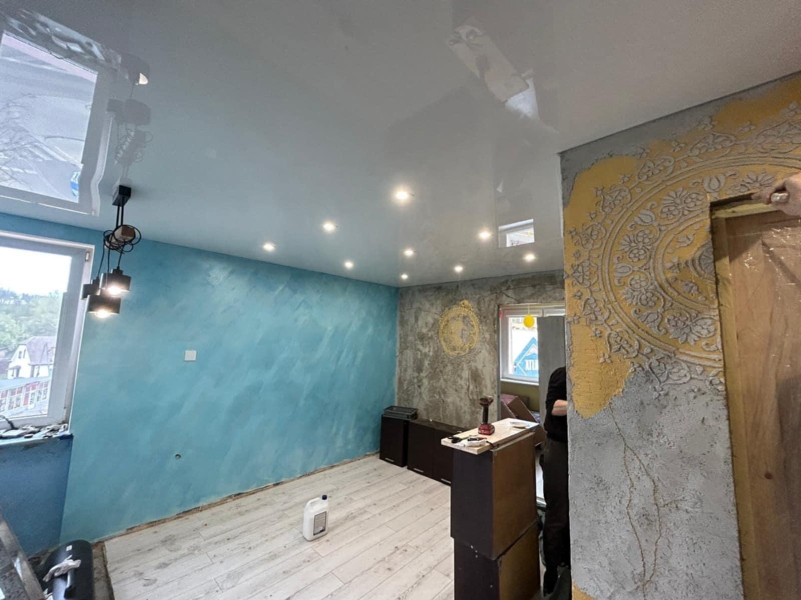 Wykończone wnętrze z błyszczącym sufitem napinanym, dekoracyjną ścianą z ornamentem i turkusową ścianą. Widoczne narzędzia i materiały malarskie.