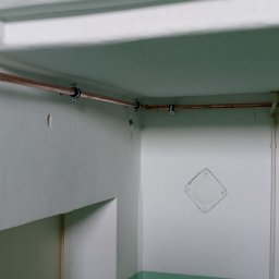 Miedziane rury instalacji gazowej zamocowane do ściany i sufitu w pomieszczeniu. Widoczne zawory i elementy przyłączeniowe. Żółte rury gazowe w tle.