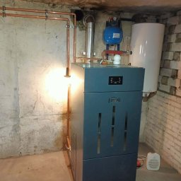 Nowoczesny piec Ferroli z instalacją CO w piwnicy. Miedziane rury, zbiornik wyrównawczy i zasobnik ciepłej wody. Oświetlenie halogenowe podkreśla detale.