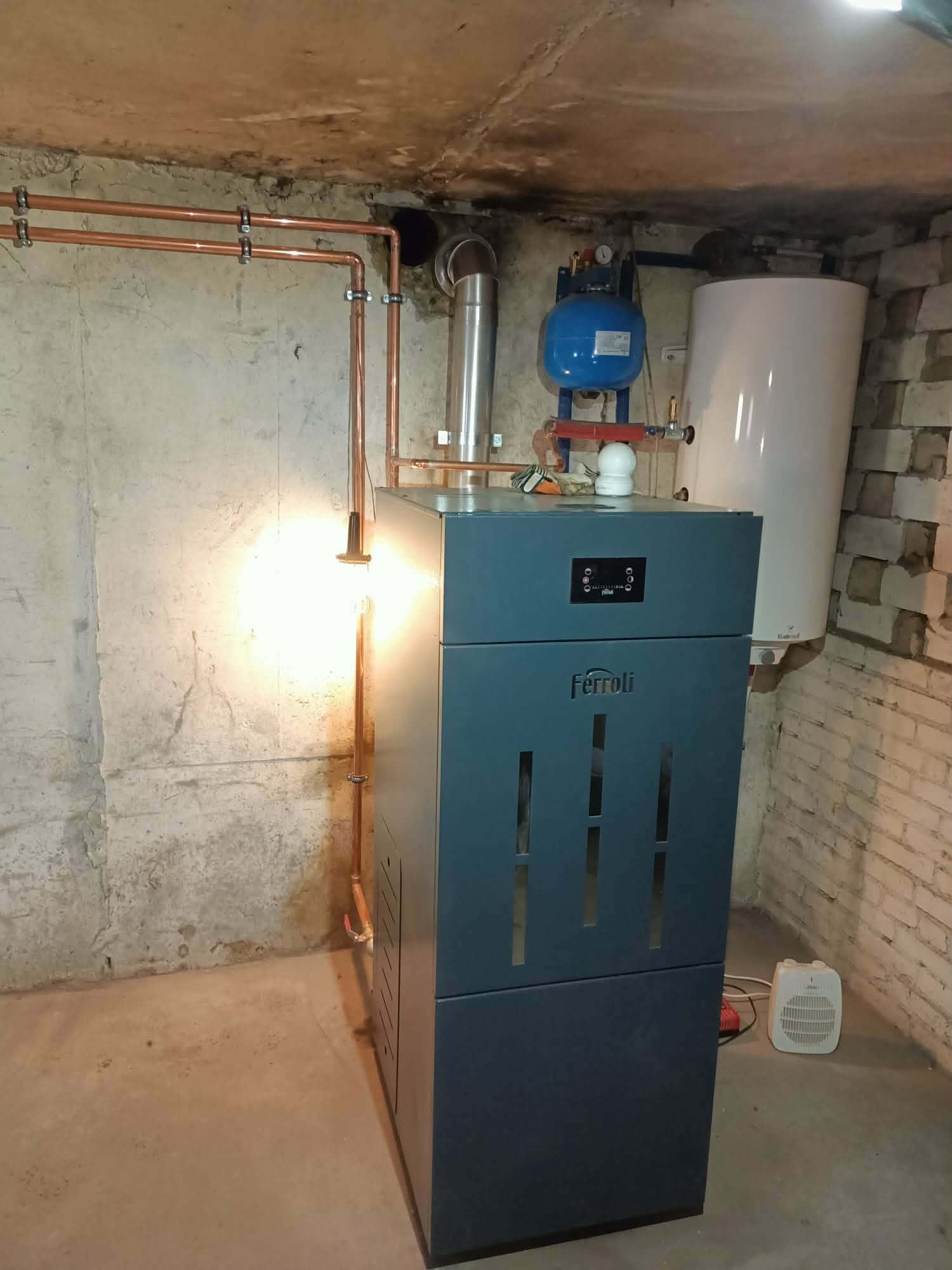 Nowoczesny piec Ferroli z instalacją CO w piwnicy. Miedziane rury, zbiornik wyrównawczy i zasobnik ciepłej wody. Oświetlenie halogenowe podkreśla detale.