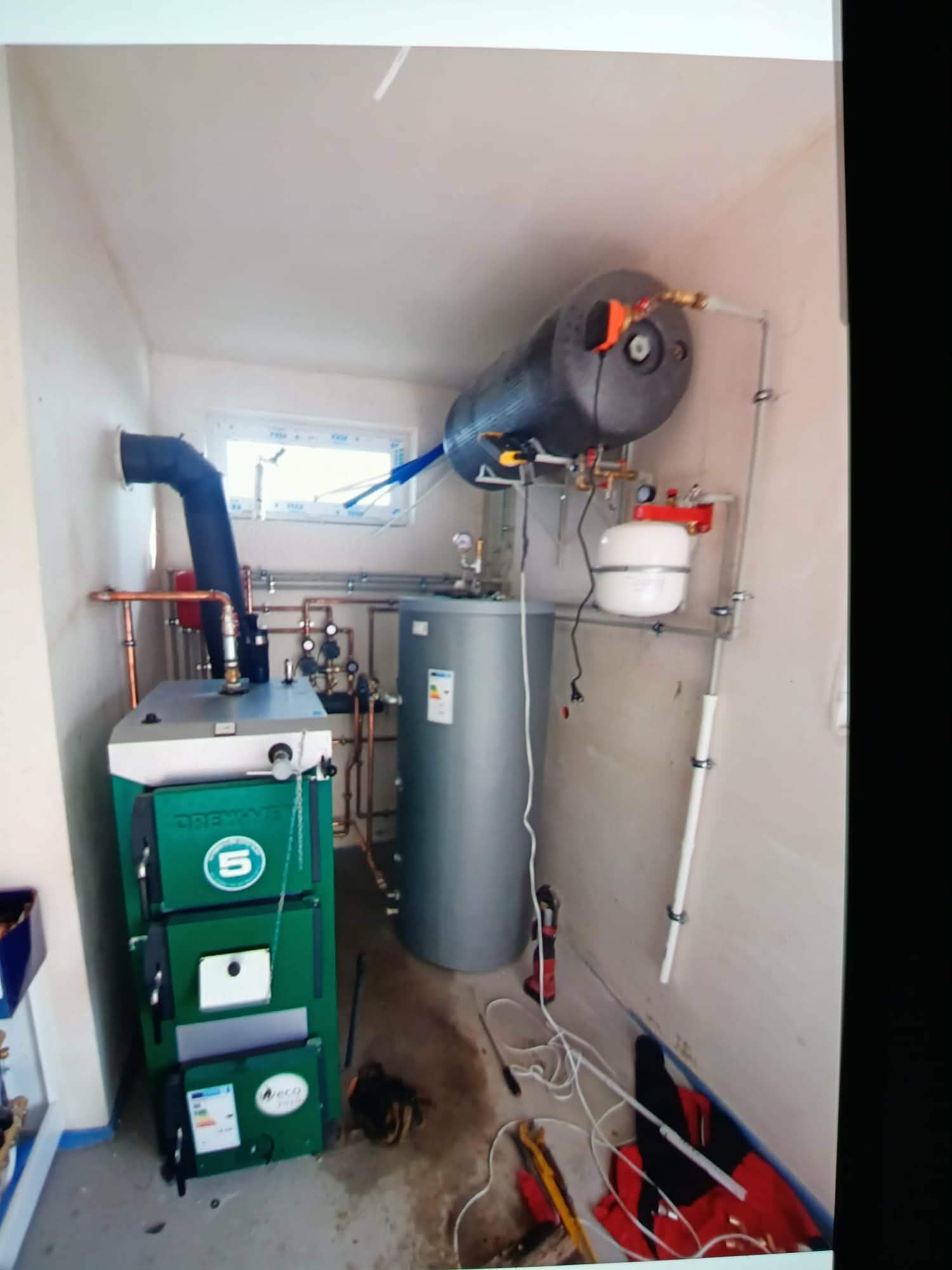 Kotłownia z piecem na paliwo stałe, zbiornikiem akumulacyjnym i zasobnikiem CWU. Widoczne rury instalacji grzewczej i osprzęt.