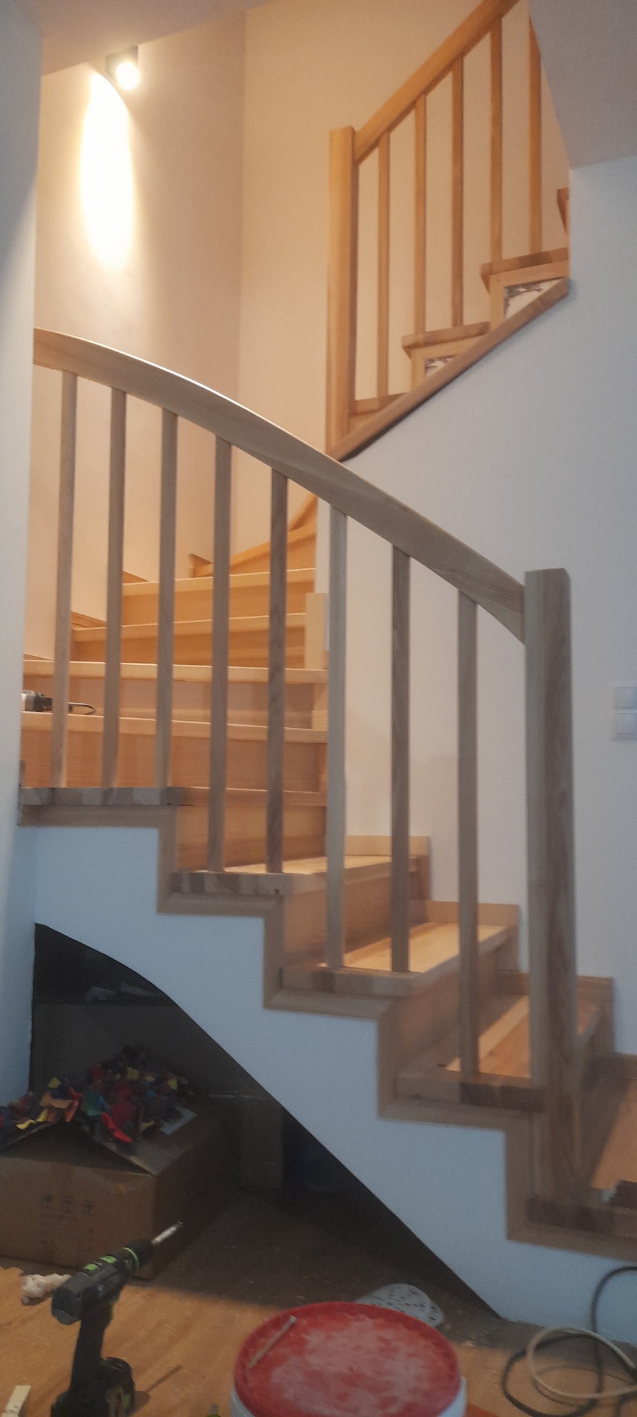 Jasne, drewniane schody z balustradą w nowoczesnym wnętrzu. Widoczne narzędzia pracy, co sugeruje etap montażu lub wykończenia. Ujęcie z dołu, podkreślające konstrukcję.