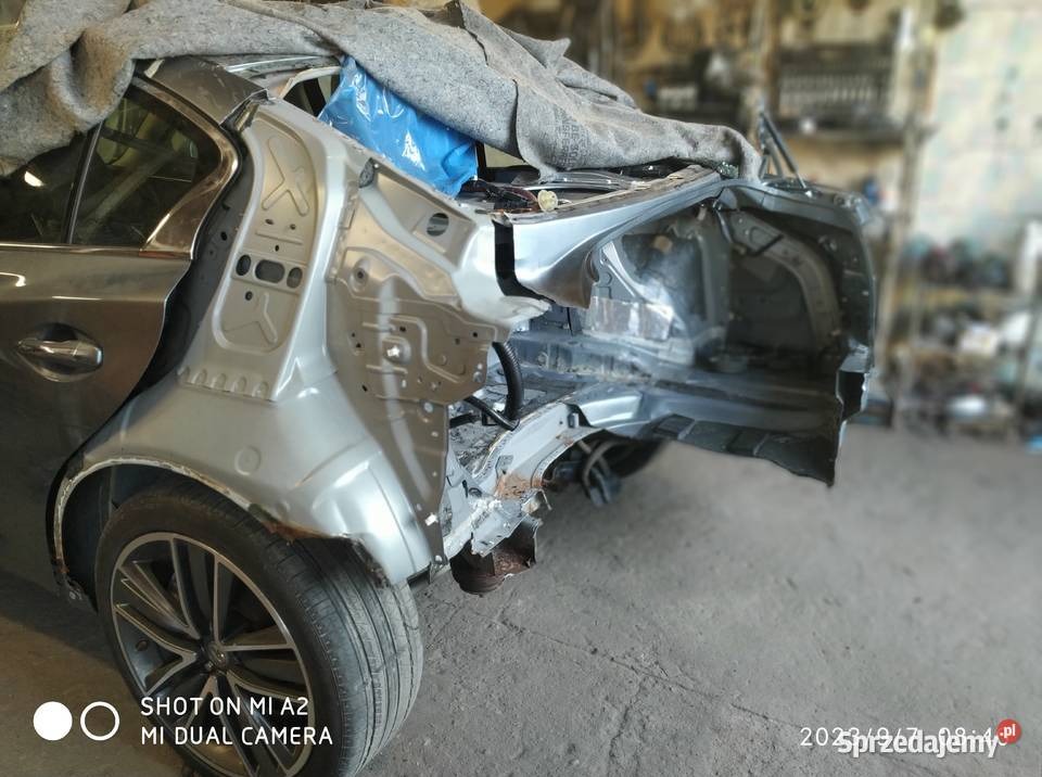 Uszkodzony tył srebrnego samochodu w warsztacie, widoczne elementy konstrukcyjne po demontażu karoserii, przygotowanie do naprawy blacharskiej.