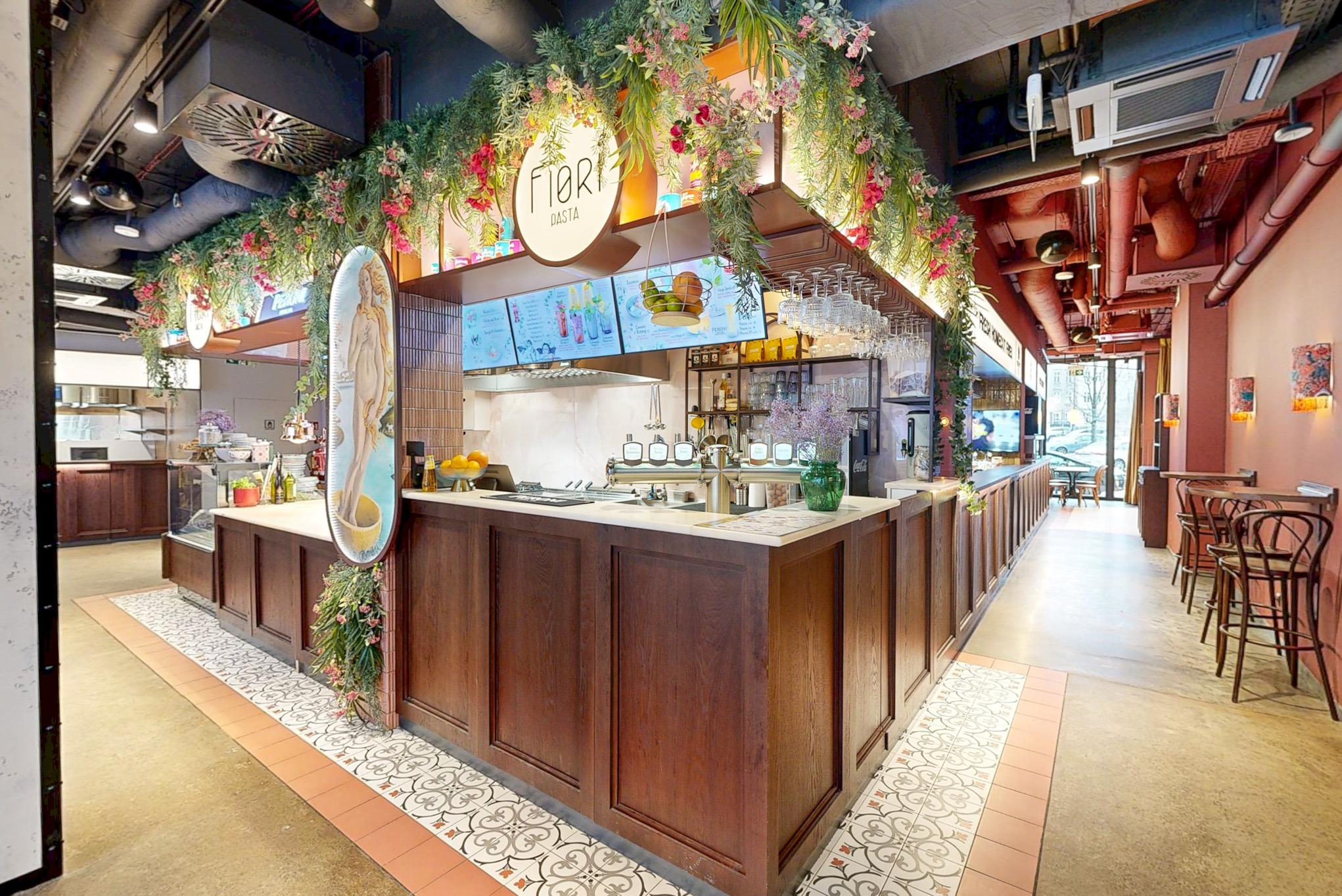 Wnętrze restauracji Fiori Pasta z drewnianym barem, kwiatowymi dekoracjami i elementami wystroju w stylu vintage. Widok na salę i kuchnię.