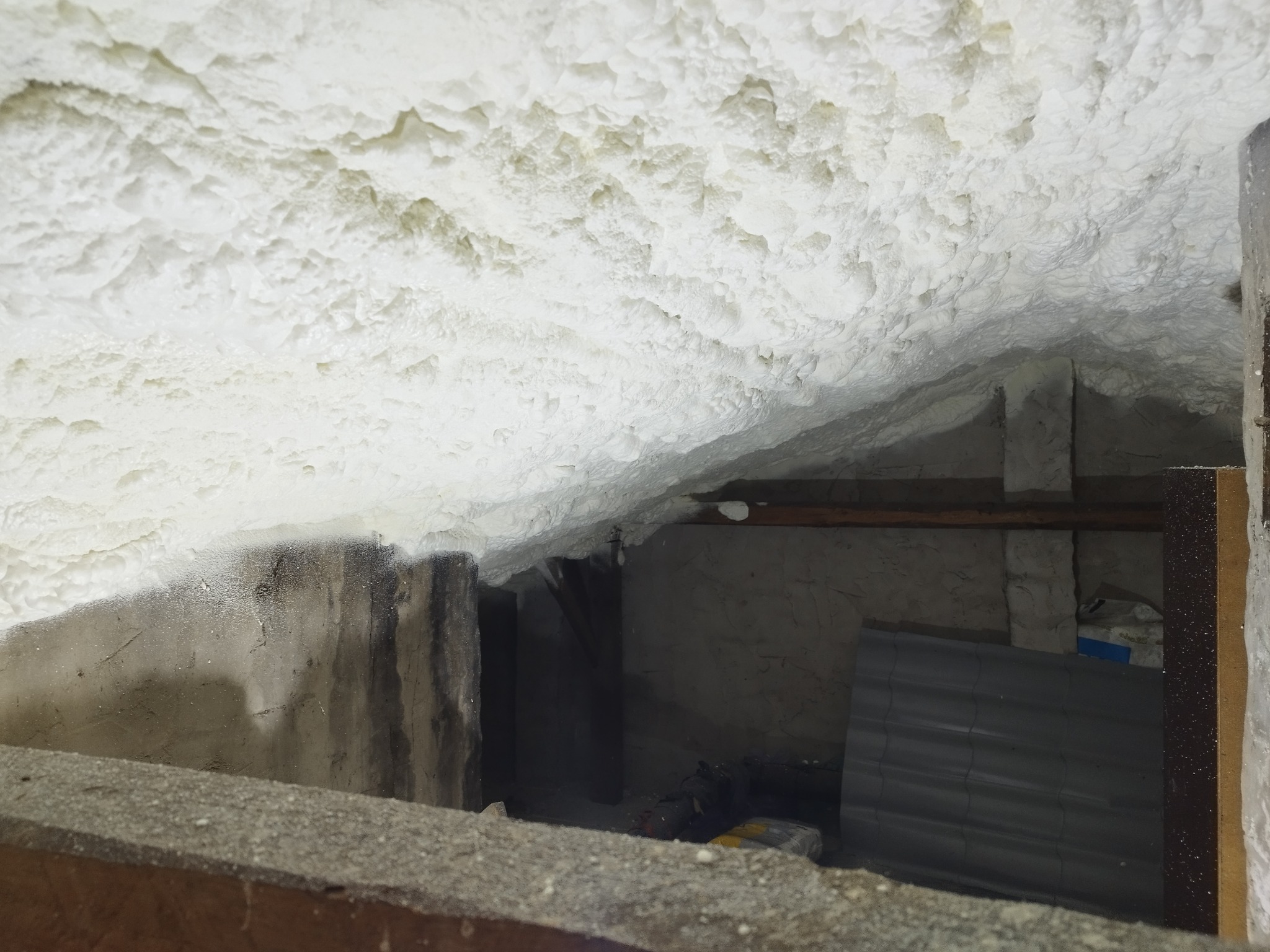 Poddasze po izolacji: biała pianka PUR szczelnie wypełnia przestrzeń między krokwiami, widoczne elementy konstrukcji dachu i fragment ściany.