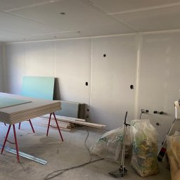Proff Tools - Wnętrze w trakcie montażu płyt kartonowo-gipsowych na ścianach i suficie. Widoczne narzędzia, materiały budowlane i stelaż pod płyty. Otwory pod instalacje elektryczne.