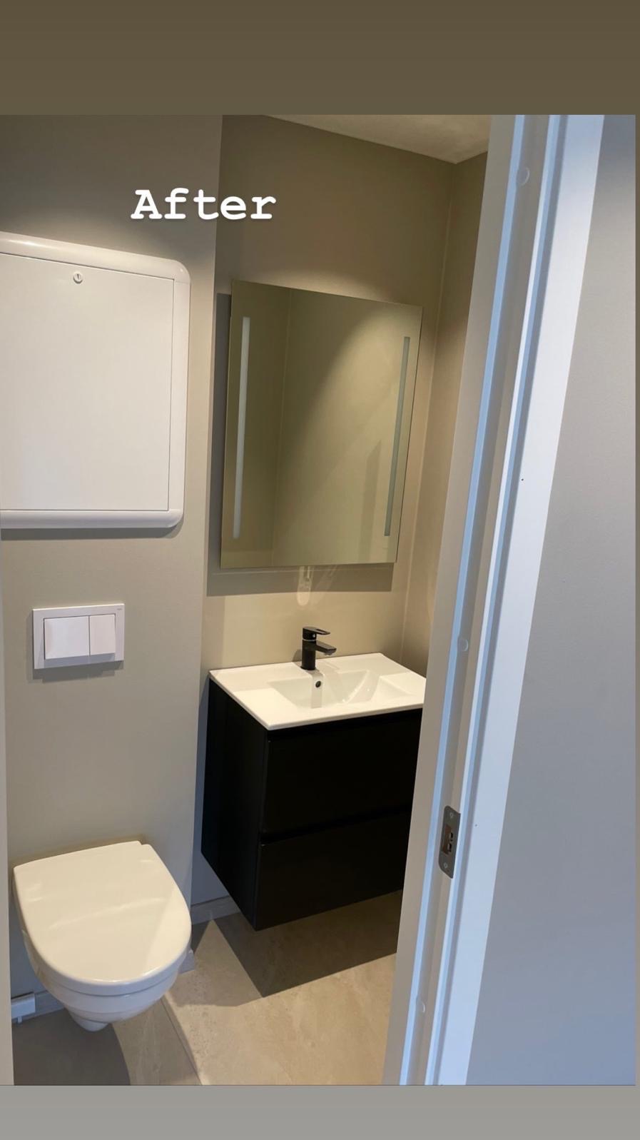 Wykończona łazienka w neutralnych barwach: podwieszana toaleta, czarna szafka z umywalką, lustro z oświetleniem LED i białe drzwi. Widok po remoncie.