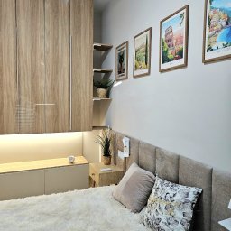 Wnętrza z pasją - Nowoczesna sypialnia z beżową zabudową meblową, podświetlanym blatem, dekoracyjnymi obrazami na ścianie i puszystym dywanem. Minimalistyczny design.