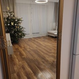Wnętrza z pasją - Parkiet ułożony w jodełkę francuską, odbity w ozdobnym lustrze w złotej ramie. W tle choinka, nowoczesne oświetlenie i minimalistyczne meble.
